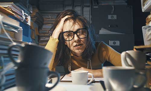 photo of a woman stressing out at a desk with a lot of books and coffee cups